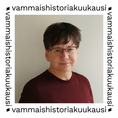 Lena tittar rakt in i kameran i en närbild. Lena har mörkt hår som når upp till pannan och öronen, rödbågade glasögon och bär en röd skjorta. Fotot är omgivet av en vit ram med texten ”vammaishistoriakuukausi” (funkishistorisk månad).