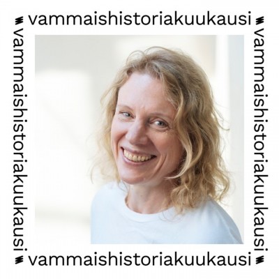  Susanne tittar in i kameran med ett leende. Hon har blont, lätt lockigt hår som når axeln och bär en vit t-shirt. Fotot är omgivet av en vit ram med texten ”vammaishistoriakuukausi” (funkishistorisk månad).