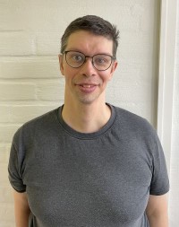 Aapolla has white skin, short brown hair, glasses and grey t-shirt.